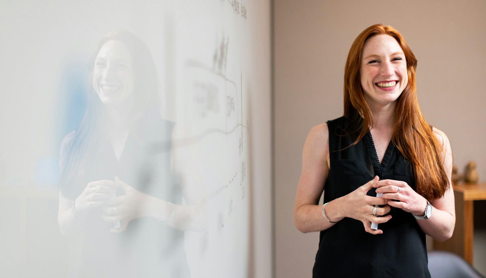 smiling woman in blue sleevless corporate top standing beside white board wearing fashion rings