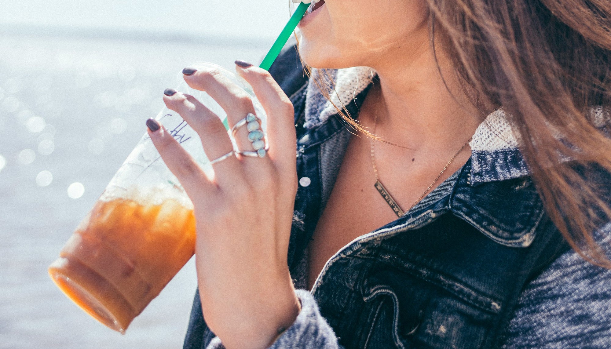 woman's hand wearing a cocktail ring and holding a cup of iced coffee with a straw