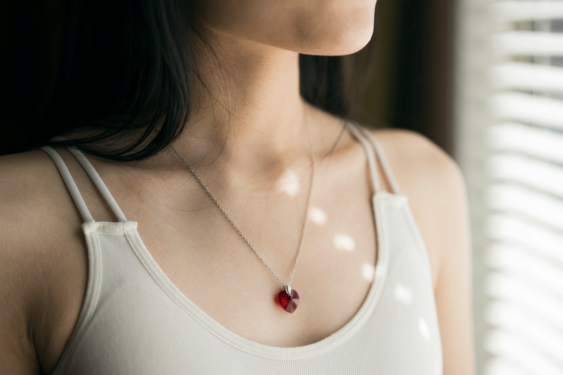 woman wearing a white tank top and a red swarovski crystal pendant necklace